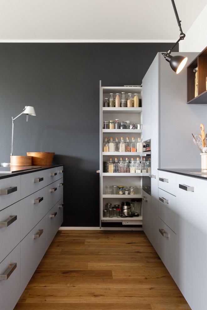 Foto de cocina actual de tamaño medio con armarios con paneles lisos, puertas de armario grises, península, encimeras negras y suelo de madera clara