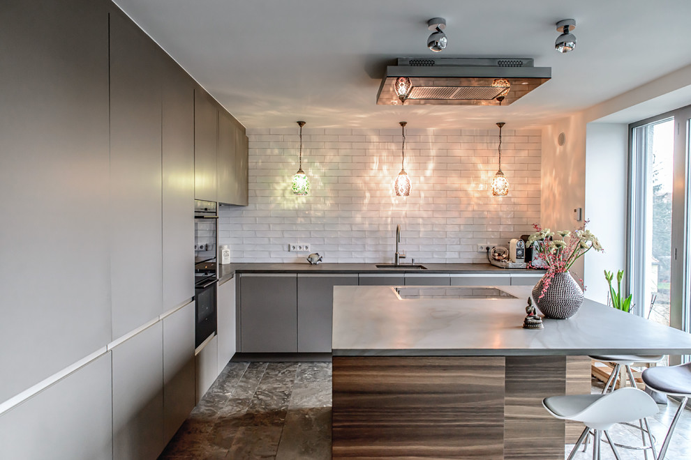 Large contemporary l-shaped enclosed kitchen in Munich with a single-bowl sink, flat-panel cabinets, grey cabinets, white splashback, metro tiled splashback, black appliances and an island.