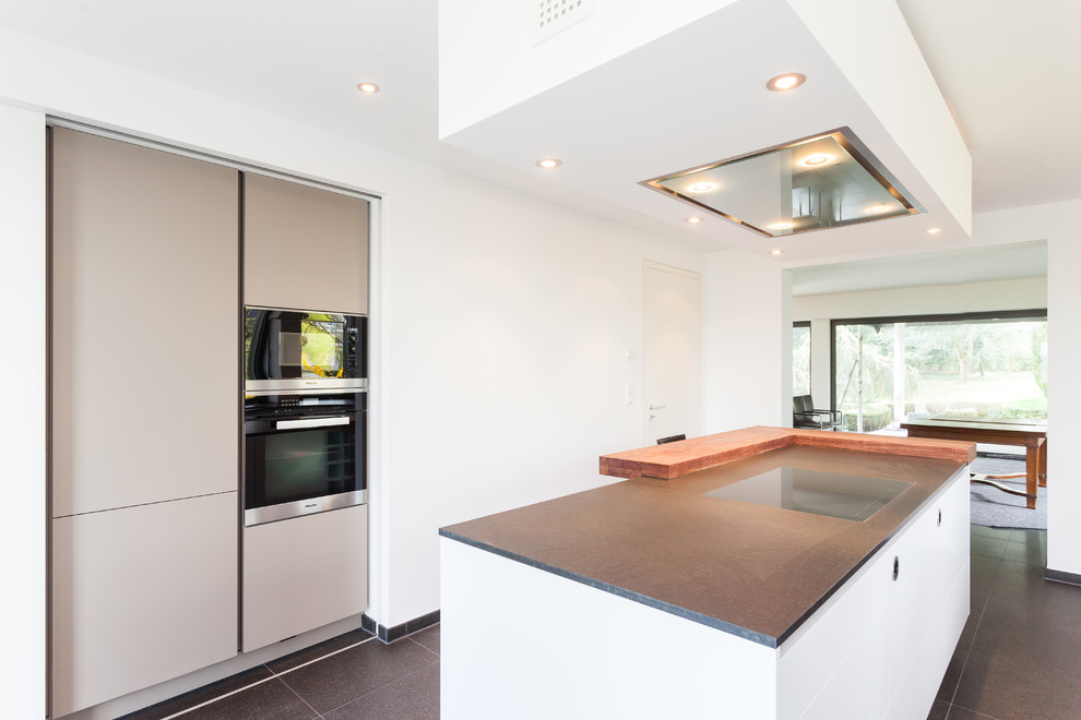 Foto de cocina contemporánea abierta con puertas de armario blancas, encimera de madera, salpicadero blanco, electrodomésticos negros y una isla