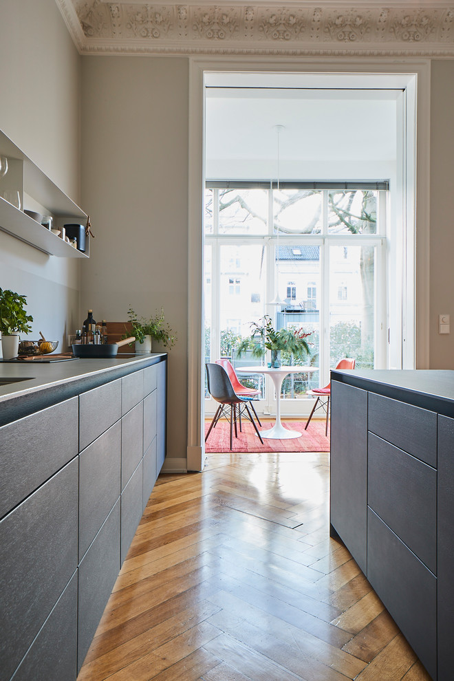 Modern inredning av ett stort grå linjärt grått kök med öppen planlösning, med en nedsänkt diskho, släta luckor, grå skåp, träbänkskiva, grått stänkskydd, målat trägolv, en köksö och brunt golv