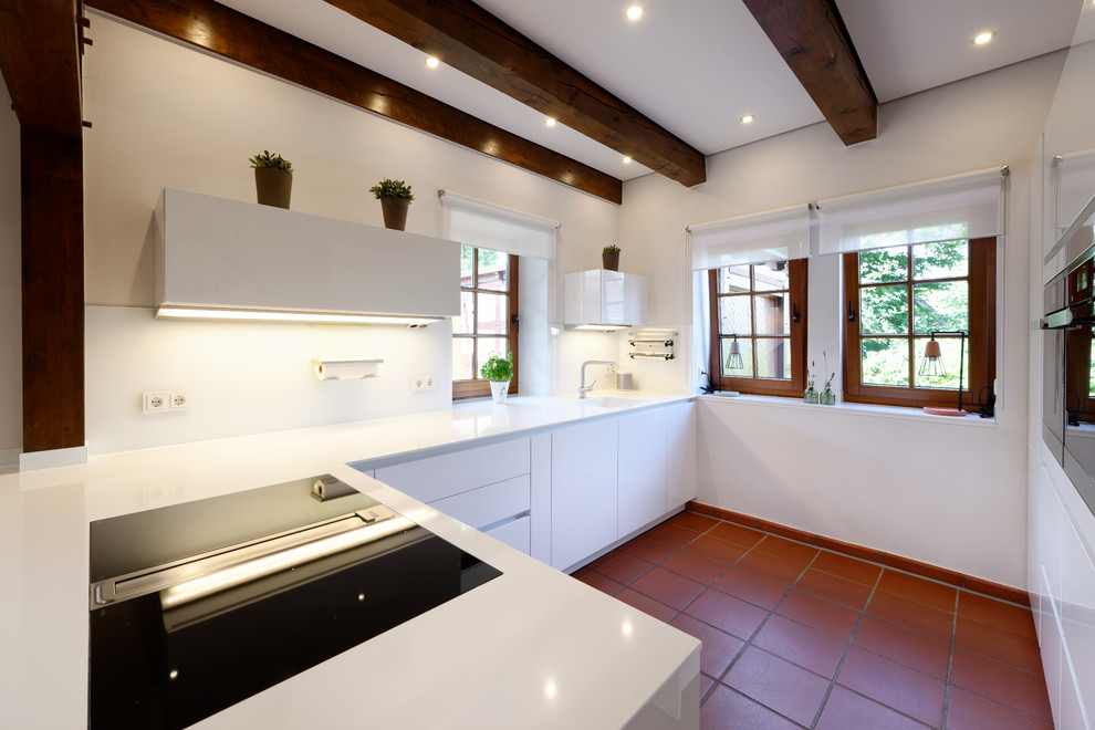 エッセンにある中くらいなカントリー風のおしゃれなキッチン (一体型シンク、フラットパネル扉のキャビネット、白いキャビネット、白いキッチンパネル、ガラス板のキッチンパネル、黒い調理設備、テラコッタタイルの床、赤い床、白いキッチンカウンター) の写真