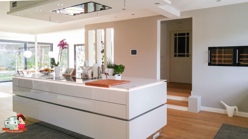 Diseño de cocina contemporánea grande abierta con puertas de armario blancas, una isla, encimera de cuarcita, electrodomésticos negros, suelo de madera clara y suelo marrón