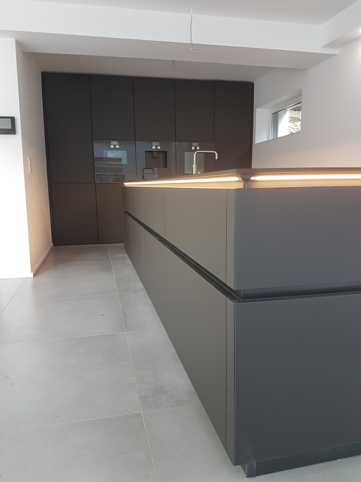 Large contemporary galley open plan kitchen in Dortmund with an integrated sink, flat-panel cabinets, black cabinets, black appliances, an island and black worktops.