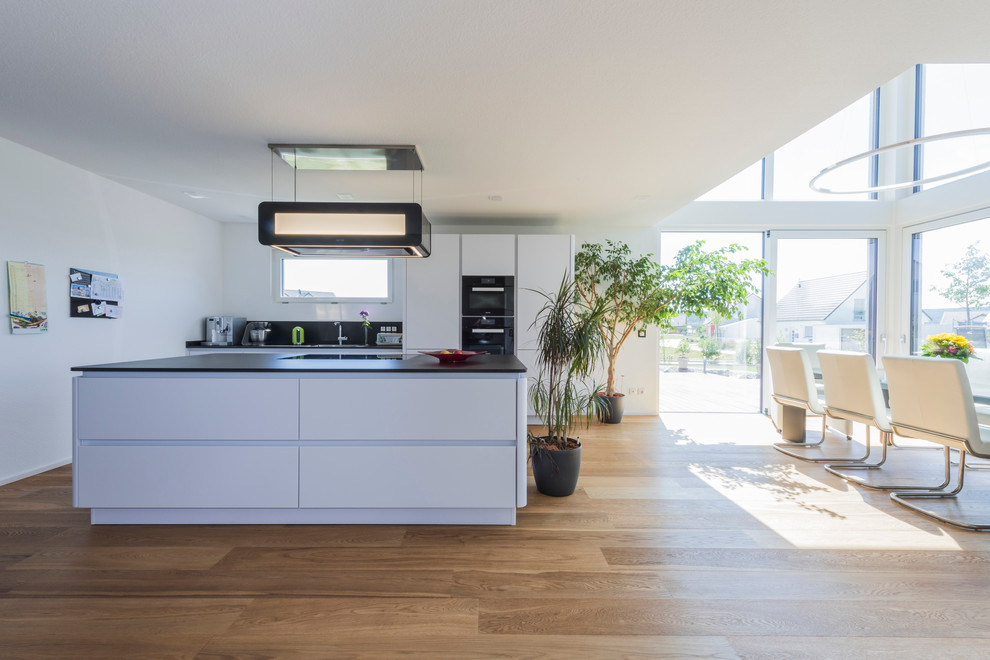 Idéer för ett modernt kök och matrum, med släta luckor, vita skåp, granitbänkskiva, svarta vitvaror, en köksö och ljust trägolv
