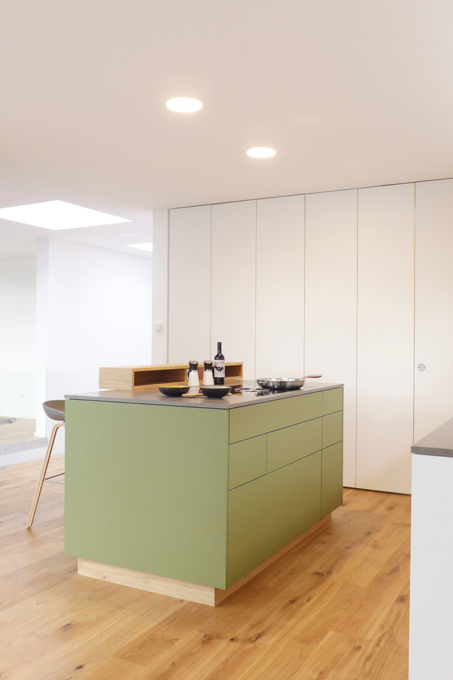Exempel på ett litet minimalistiskt grå grått kök, med en undermonterad diskho, släta luckor, gröna skåp, bänkskiva i kvarts, vitt stänkskydd, stänkskydd i trä, svarta vitvaror, mellanmörkt trägolv, en köksö och brunt golv