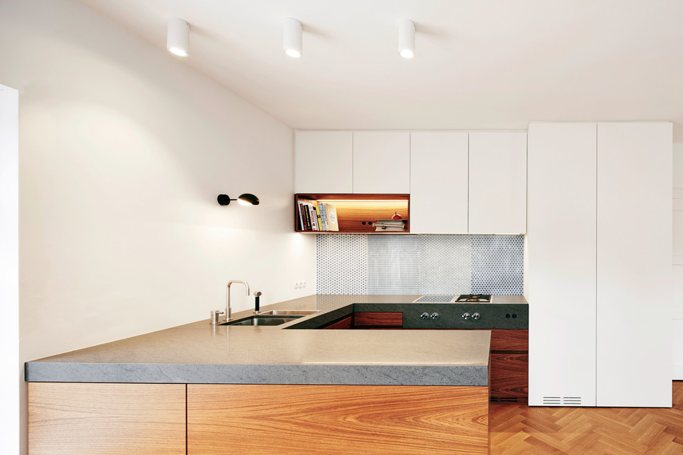Exempel på ett litet modernt kök, med en dubbel diskho, släta luckor, vita skåp, stänkskydd i mosaik, ljust trägolv, blått stänkskydd, integrerade vitvaror och en halv köksö