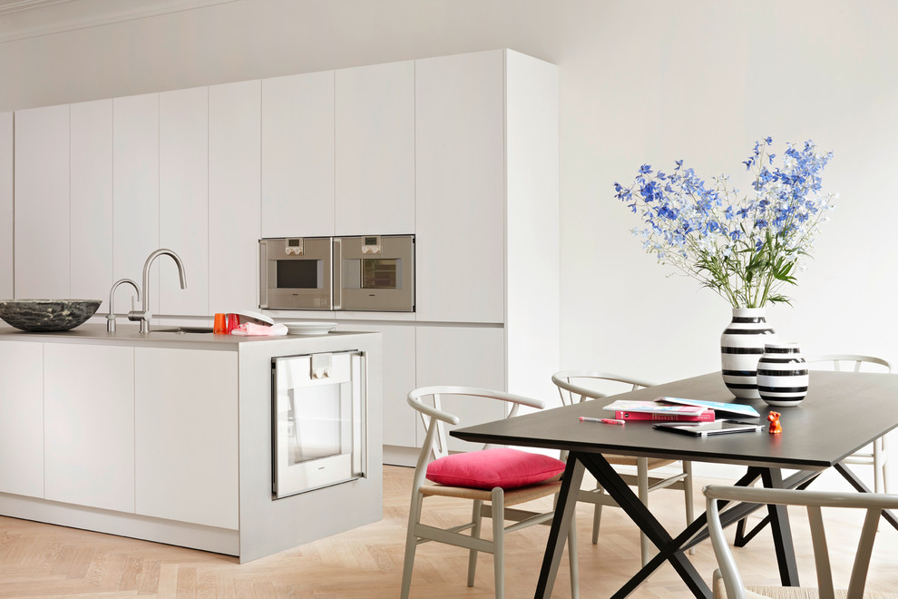 ハンブルクにある広い北欧スタイルのおしゃれなキッチン (フラットパネル扉のキャビネット、白いキャビネット、淡色無垢フローリング、シルバーの調理設備、ステンレスカウンター) の写真