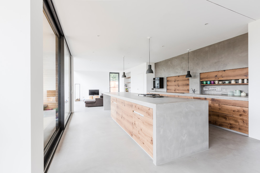 Bild på ett mycket stort funkis kök, med en nedsänkt diskho, släta luckor, skåp i mellenmörkt trä, bänkskiva i betong, grått stänkskydd, betonggolv och en köksö
