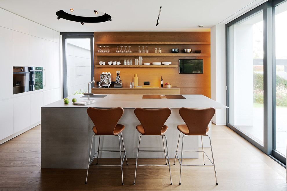 Bild på ett mellanstort funkis grå grått kök, med en integrerad diskho, släta luckor, vita skåp, bänkskiva i rostfritt stål, brunt stänkskydd, stänkskydd i trä, svarta vitvaror, målat trägolv, en köksö och brunt golv