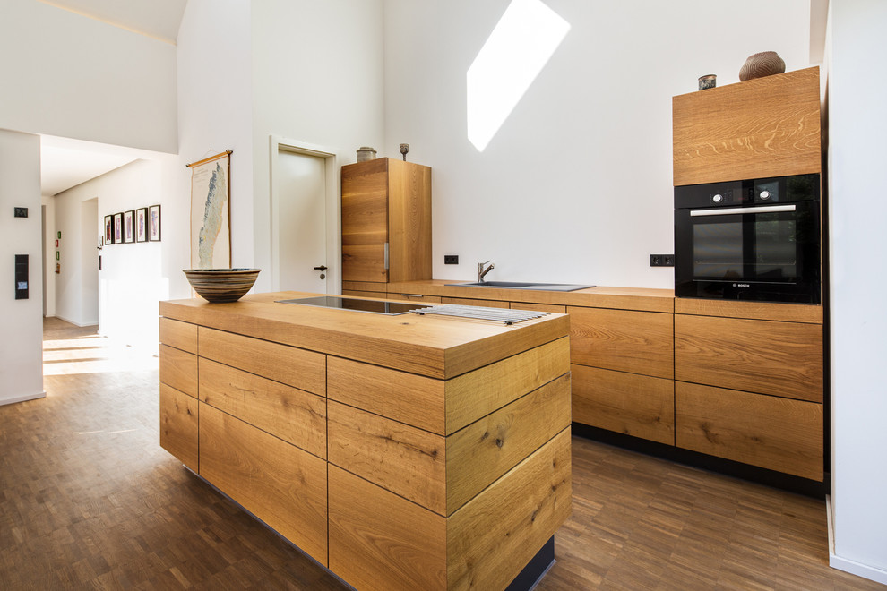Photo of a medium sized contemporary open plan kitchen in Hamburg with a built-in sink, flat-panel cabinets, medium wood cabinets, wood worktops, white splashback, integrated appliances, medium hardwood flooring, an island and brown floors.