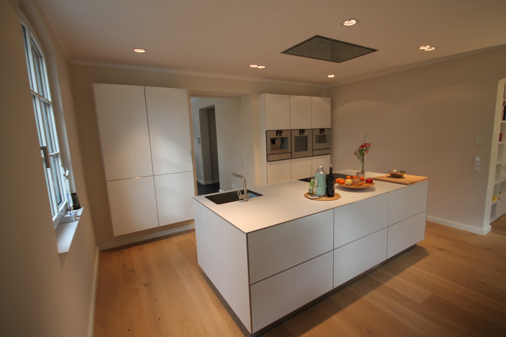 Ejemplo de cocina lineal clásica abierta con puertas de armario blancas, electrodomésticos de acero inoxidable y una isla