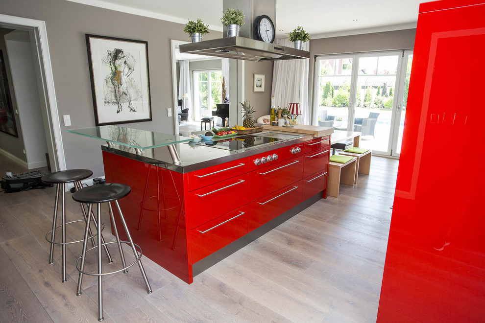 Modelo de cocina actual abierta con puertas de armario rojas, encimera de acero inoxidable, electrodomésticos negros y una isla