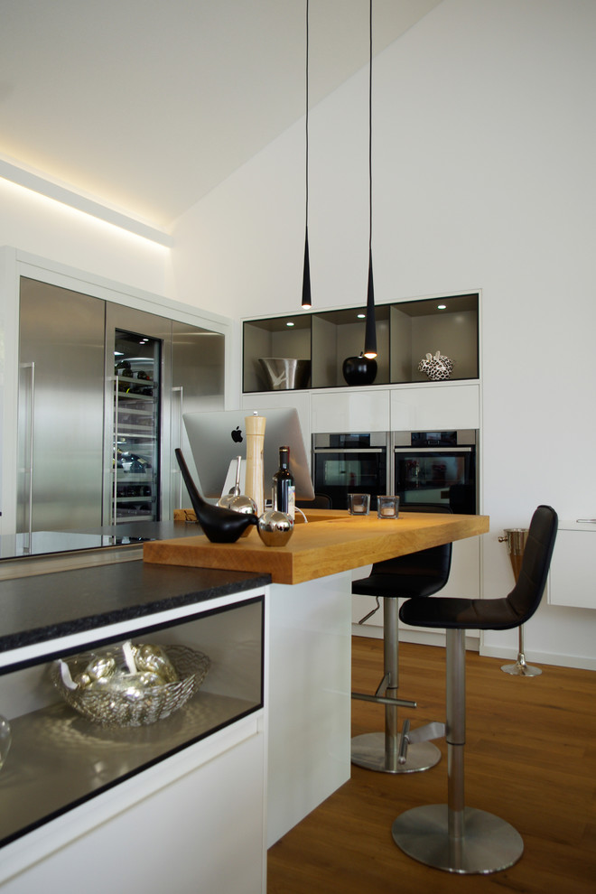 Moderne Küche mit Arbeitsplatte aus Holz, Küchengeräten aus Edelstahl, braunem Holzboden und Kücheninsel in Sonstige