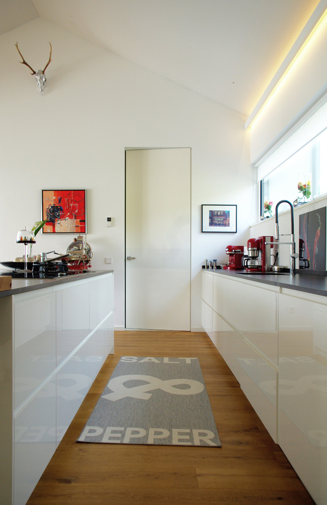 Zweizeilige, Mittelgroße Moderne Küche mit Unterbauwaschbecken, flächenbündigen Schrankfronten, weißen Schränken, braunem Holzboden und Kücheninsel in Sonstige