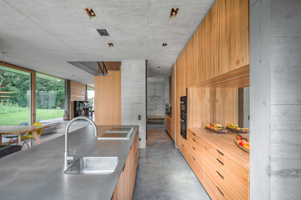 This is an example of an urban galley kitchen in Munich with an integrated sink, flat-panel cabinets, medium wood cabinets, mirror splashback, concrete flooring, an island, grey floors and grey worktops.