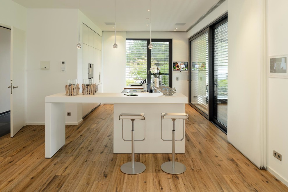 Cette image montre une grande cuisine ouverte design avec un placard à porte plane, des portes de placard blanches, un électroménager blanc, parquet clair, îlot et un évier encastré.