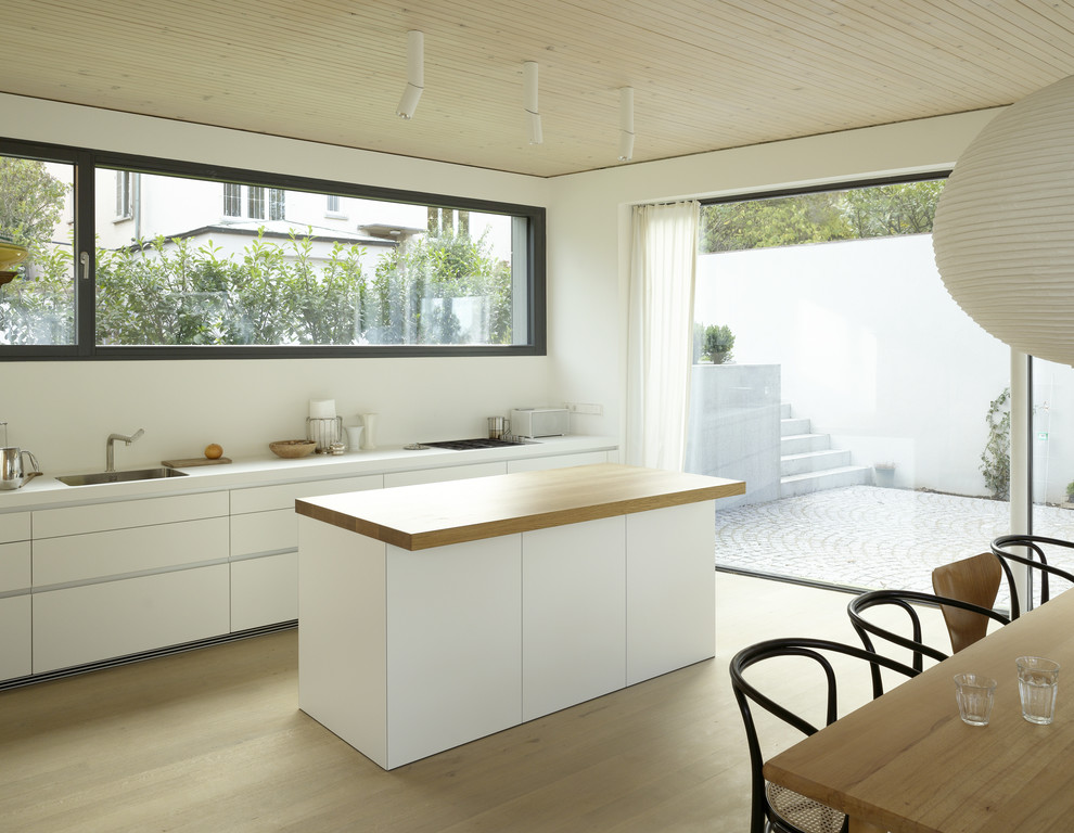 Einzeilige, Mittelgroße Moderne Küche mit Unterbauwaschbecken, flächenbündigen Schrankfronten, weißen Schränken, Küchenrückwand in Weiß, braunem Holzboden und Kücheninsel in Stuttgart