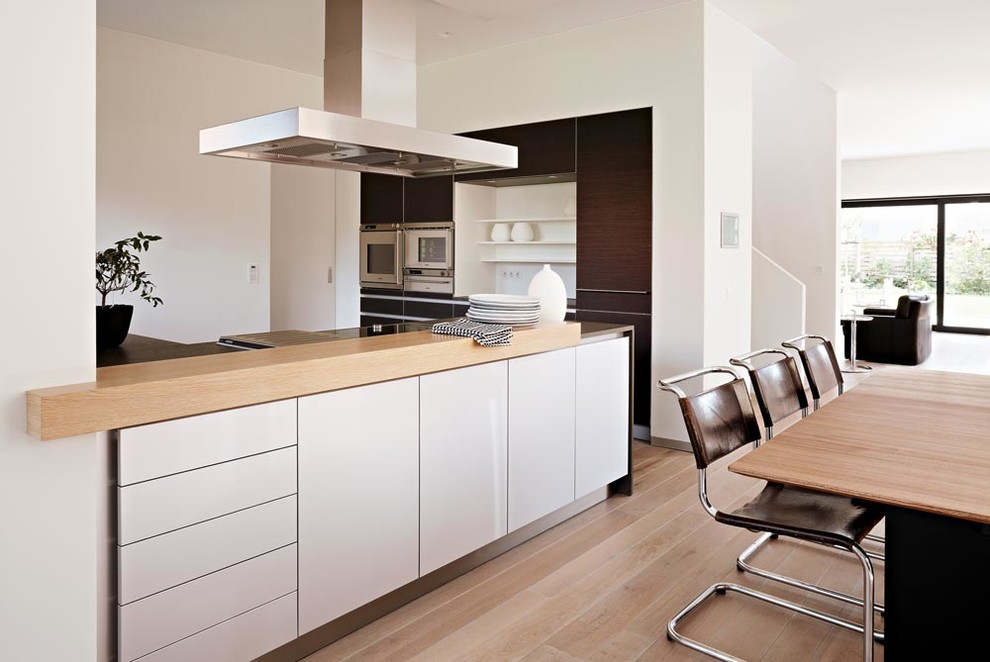 Medium sized contemporary open plan kitchen in Hamburg with flat-panel cabinets, dark wood cabinets, integrated appliances, medium hardwood flooring and a breakfast bar.