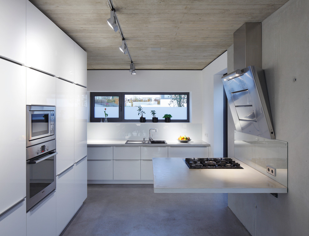 Design ideas for a large contemporary enclosed kitchen in Dortmund with a built-in sink, flat-panel cabinets, white cabinets, concrete flooring, concrete worktops, grey splashback, glass sheet splashback and stainless steel appliances.