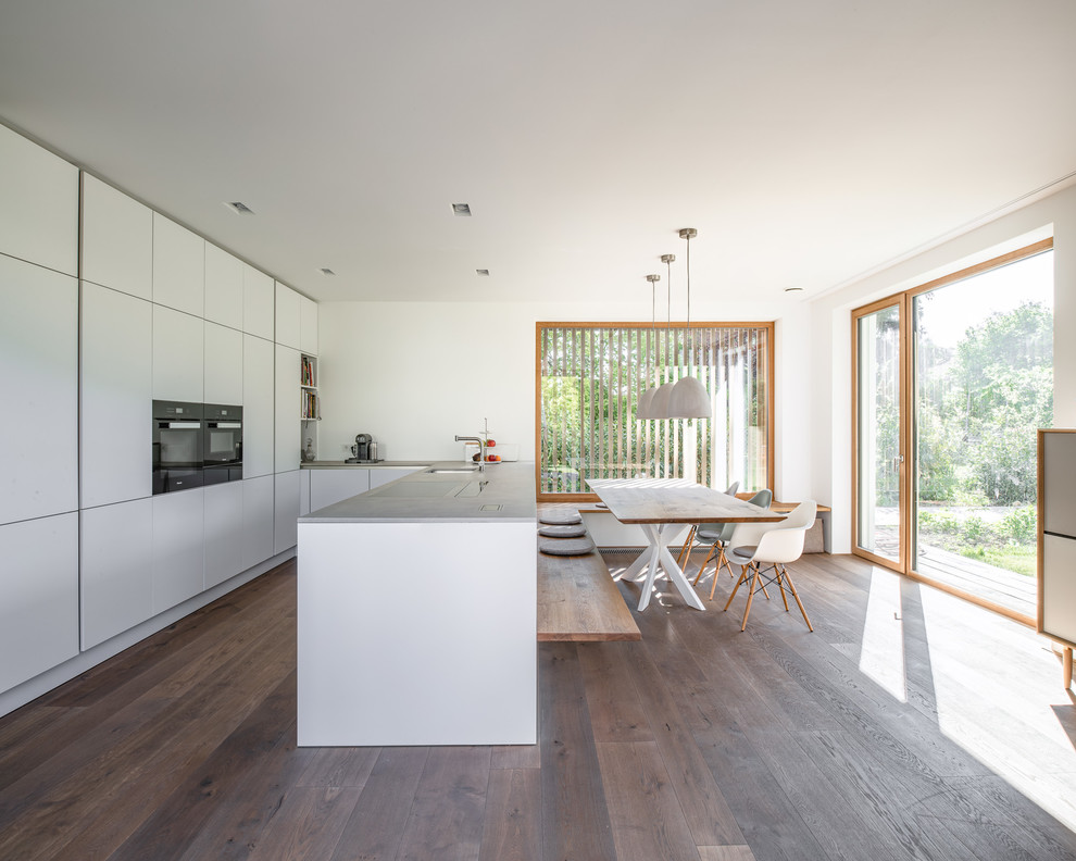 Idéer för ett modernt grå kök, med en undermonterad diskho, släta luckor, vita skåp, svarta vitvaror, mellanmörkt trägolv, en halv köksö och brunt golv