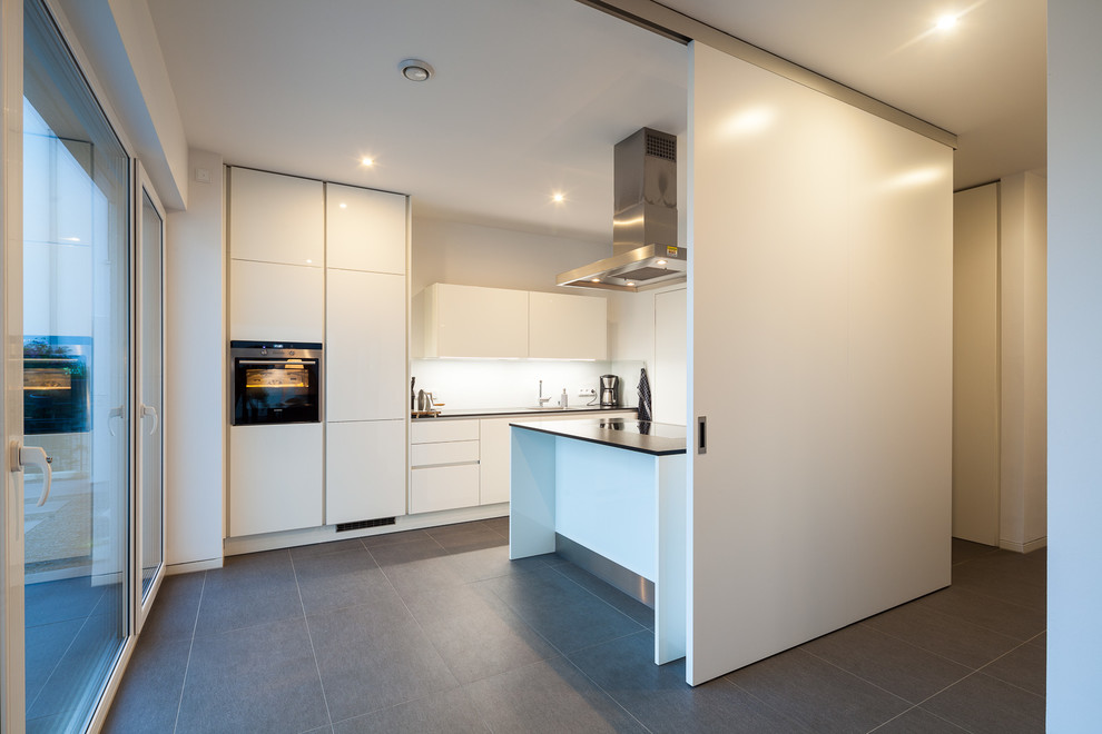 Offene Moderne Küche mit weißen Schränken, Küchenrückwand in Weiß und grauem Boden in Köln