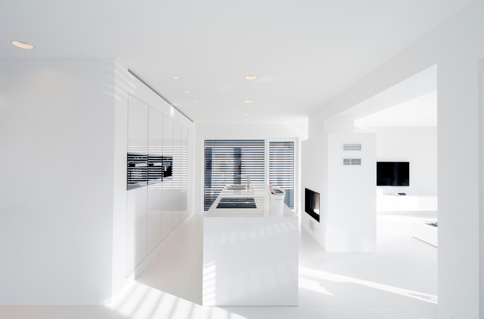 Modelo de cocina contemporánea grande abierta con armarios con paneles lisos, puertas de armario blancas, electrodomésticos negros y una isla