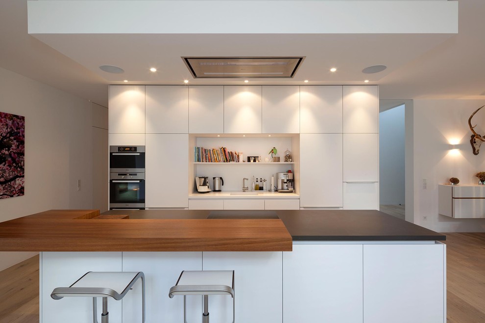 Esempio di una cucina design di medie dimensioni con lavello integrato, ante lisce, ante bianche, elettrodomestici da incasso, pavimento in legno massello medio e paraspruzzi bianco