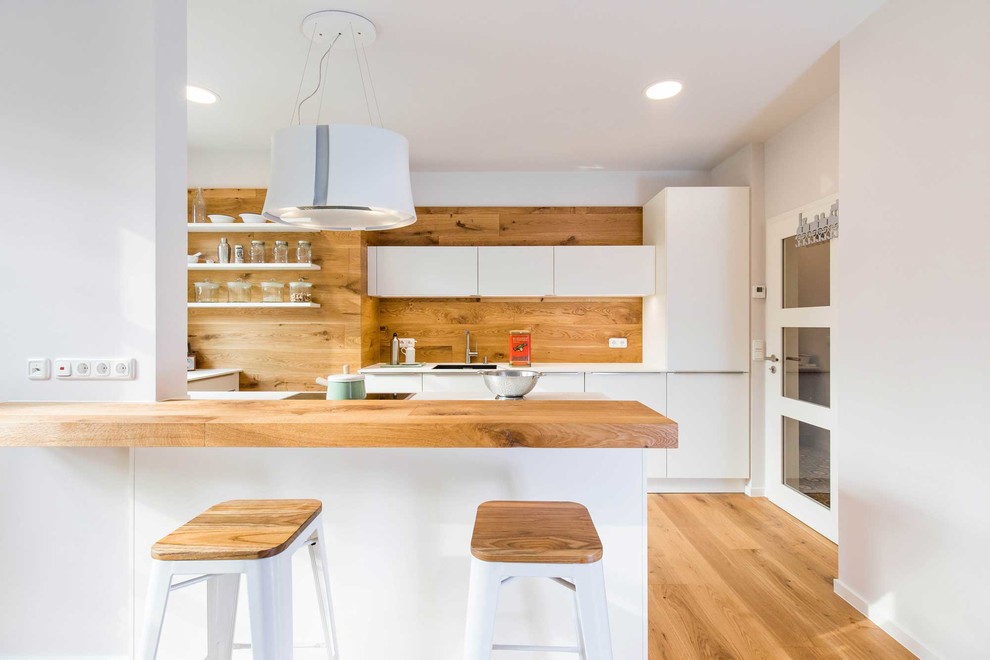 Idéer för stora minimalistiska vitt kök, med en integrerad diskho, släta luckor, vita skåp, brunt stänkskydd, stänkskydd i trä, mellanmörkt trägolv, en halv köksö och brunt golv