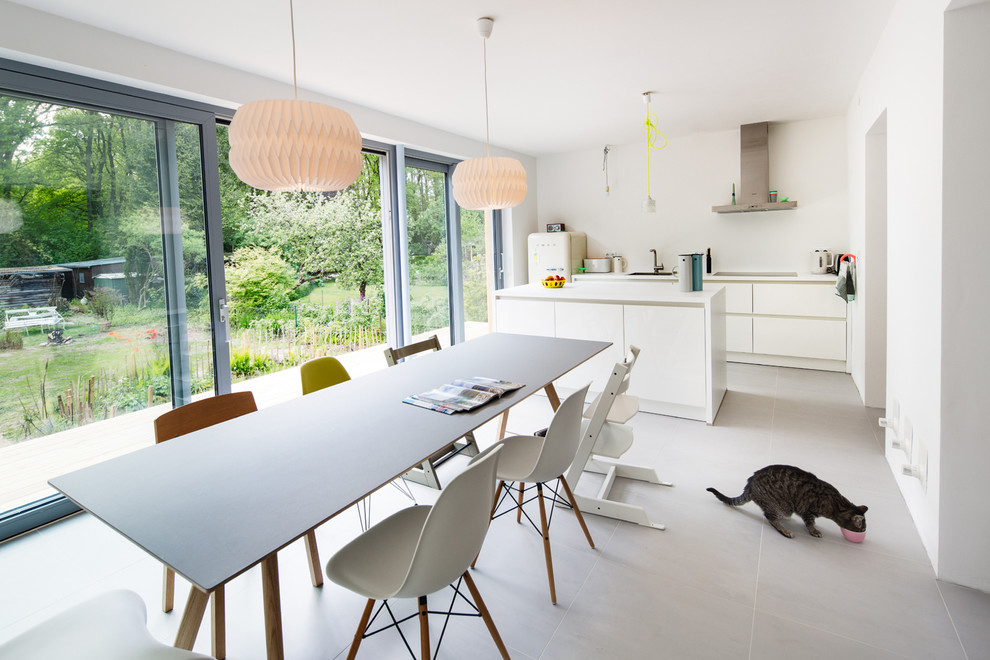 Foto på ett mellanstort funkis linjärt kök och matrum, med släta luckor, vita skåp, vitt stänkskydd, vita vitvaror, en köksö, en nedsänkt diskho och grått golv