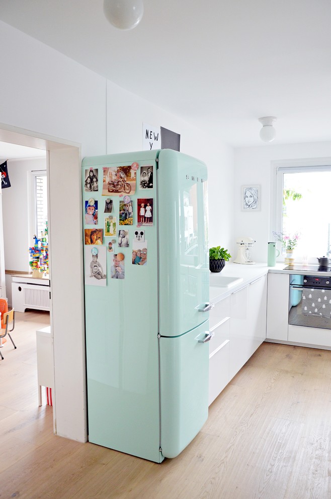 Medium sized scandinavian l-shaped kitchen/diner in Dusseldorf with flat-panel cabinets, white cabinets, light hardwood flooring, a built-in sink and coloured appliances.