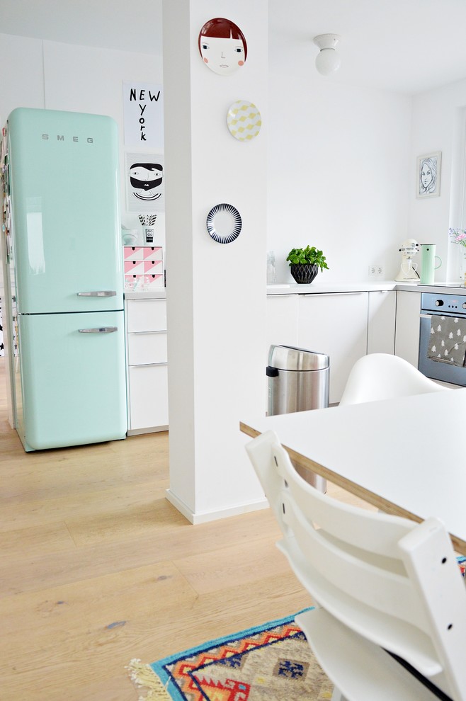 Medium sized scandi l-shaped kitchen/diner in Dusseldorf with white cabinets, white splashback, light hardwood flooring, flat-panel cabinets and coloured appliances.