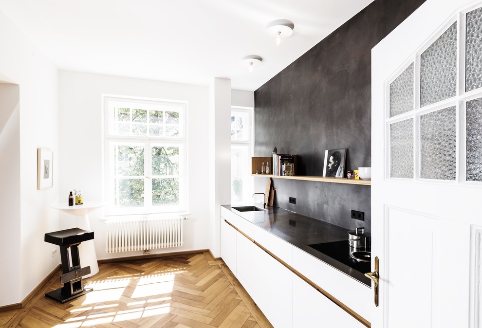 Modern inredning av ett stort linjärt kök med öppen planlösning, med en integrerad diskho, släta luckor, vita skåp, bänkskiva i rostfritt stål, svart stänkskydd, stänkskydd i kalk, svarta vitvaror, mellanmörkt trägolv och brunt golv