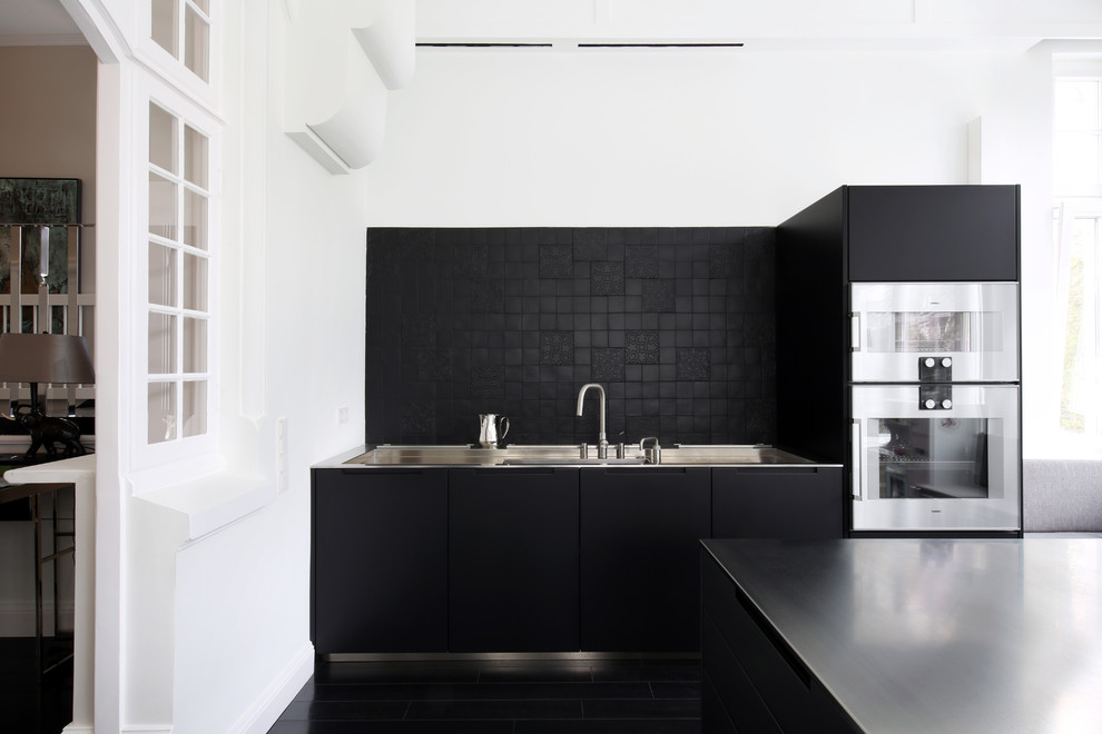 Inredning av ett modernt avskilt, stort svart linjärt svart kök, med släta luckor, svarta skåp, svart stänkskydd, rostfria vitvaror, svart golv och flera köksöar