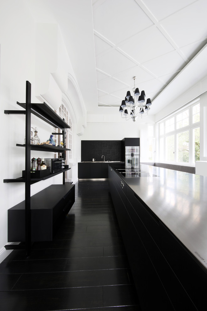 Modern inredning av ett avskilt, stort svart linjärt svart kök, med släta luckor, svarta skåp, svart stänkskydd, rostfria vitvaror, flera köksöar och svart golv