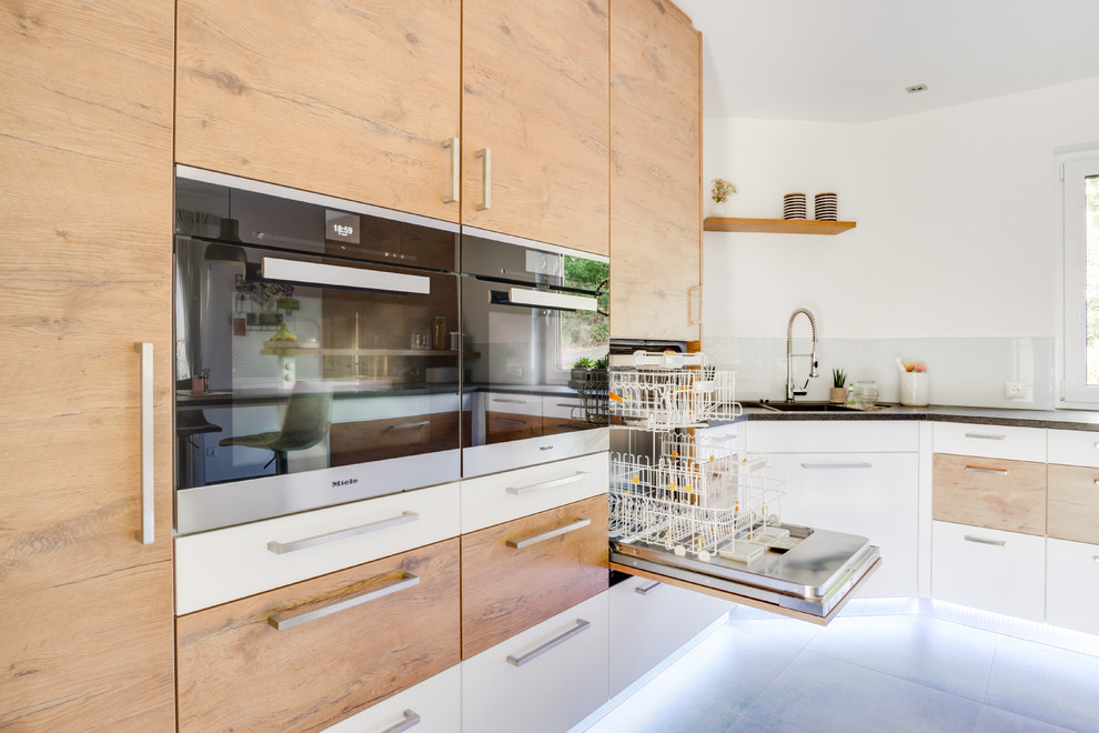 Modern inredning av ett stort grå grått kök, med en integrerad diskho, släta luckor, skåp i mellenmörkt trä, granitbänkskiva, vitt stänkskydd, stänkskydd i trä, rostfria vitvaror, cementgolv, en köksö och grått golv