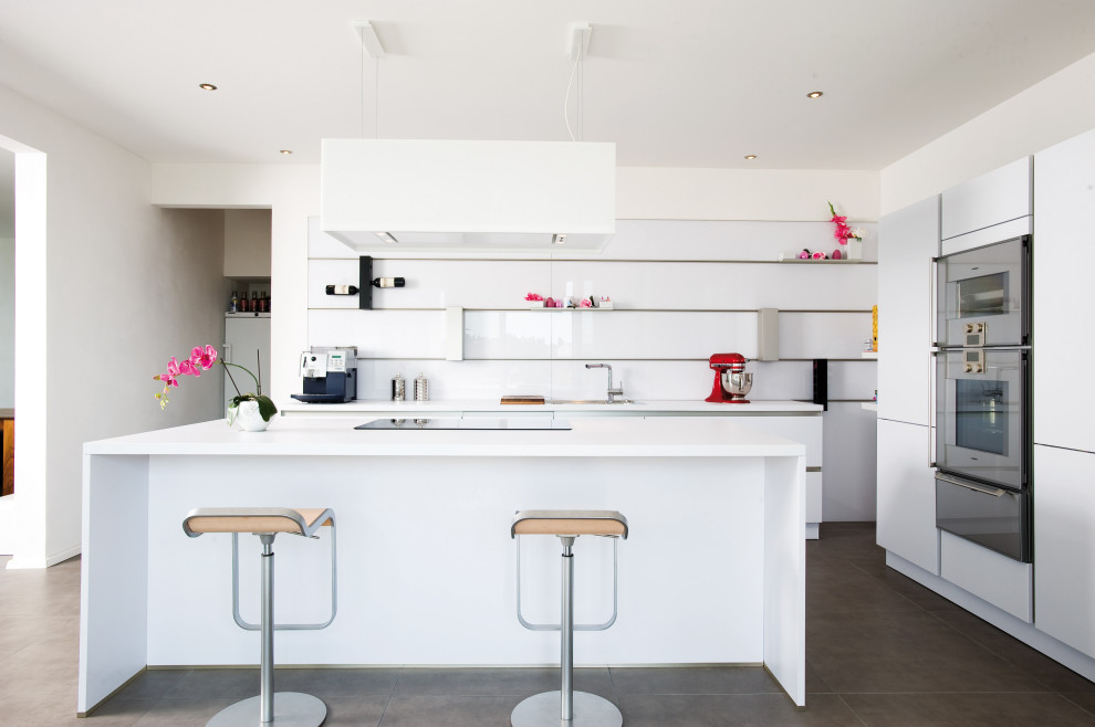 Moderne Küche in L-Form mit flächenbündigen Schrankfronten, weißen Schränken, Küchengeräten aus Edelstahl, Kücheninsel, grauem Boden und weißer Arbeitsplatte in Sonstige