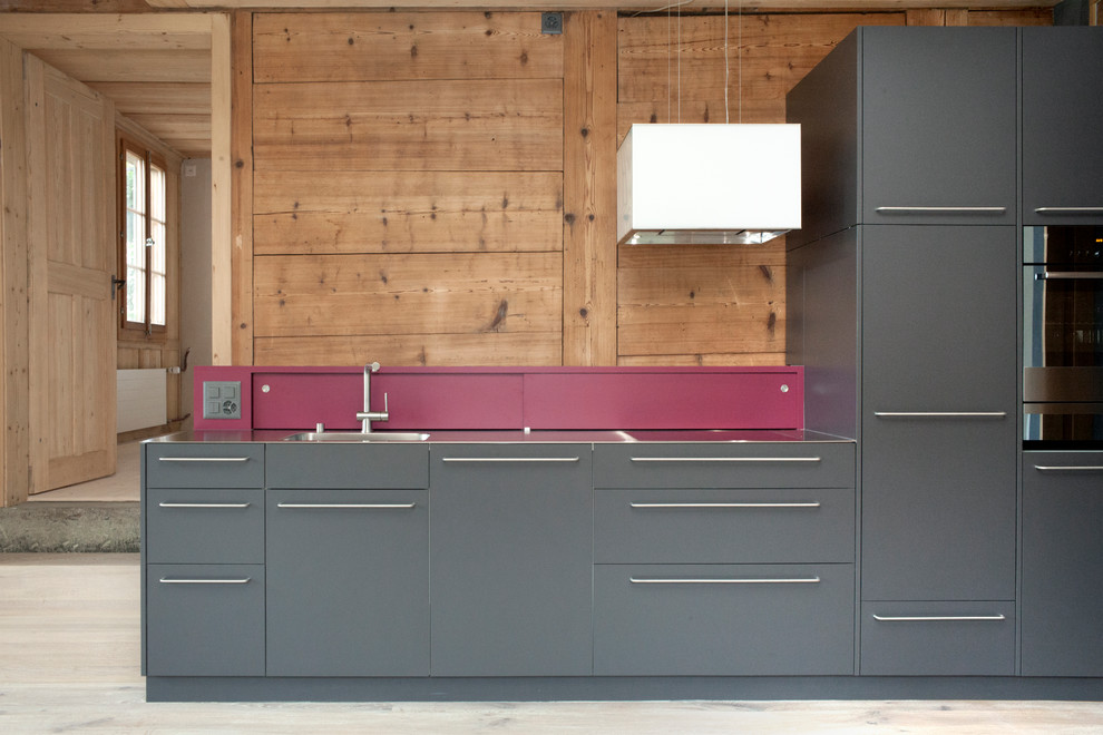 Small urban single-wall open plan kitchen in Berlin with a built-in sink, flat-panel cabinets, grey cabinets, stainless steel worktops, wood splashback, integrated appliances and painted wood flooring.