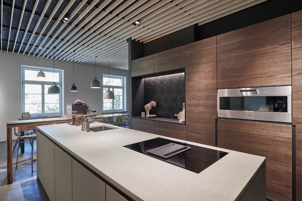 Bild på ett stort funkis grå grått kök, med en undermonterad diskho, släta luckor, skåp i mörkt trä, bänkskiva i betong, svart stänkskydd, stänkskydd i cementkakel, rostfria vitvaror, en köksö och grått golv