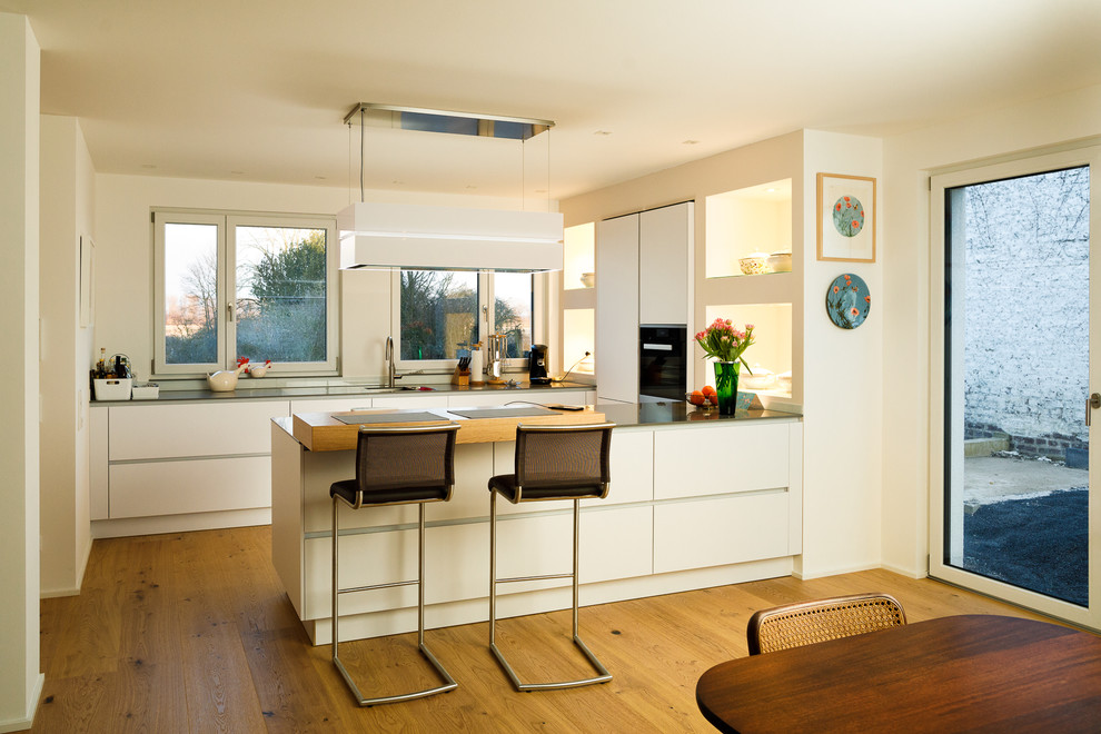 Foto på ett stort funkis grå u-kök, med släta luckor, vita skåp, rostfria vitvaror, mellanmörkt trägolv, en halv köksö och brunt golv
