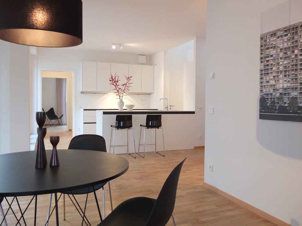 Medium sized contemporary open plan kitchen in Berlin with flat-panel cabinets, white cabinets, white splashback, medium hardwood flooring and a breakfast bar.
