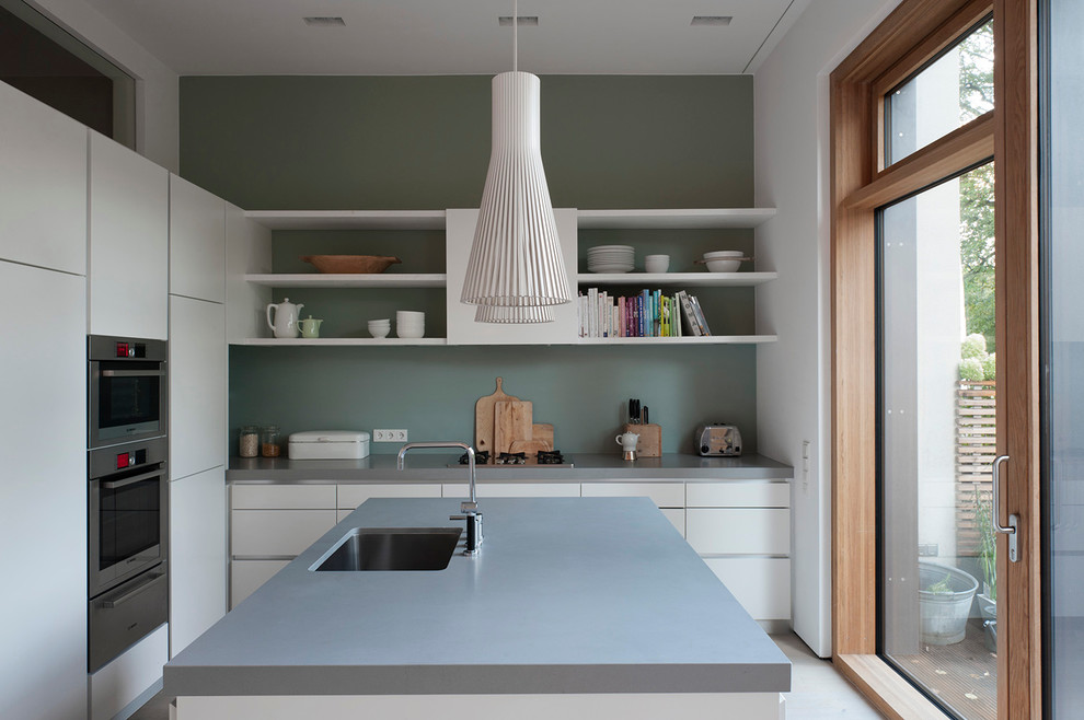 Exempel på ett avskilt, mellanstort minimalistiskt l-kök, med en köksö, en undermonterad diskho, släta luckor, vita skåp, grönt stänkskydd och rostfria vitvaror