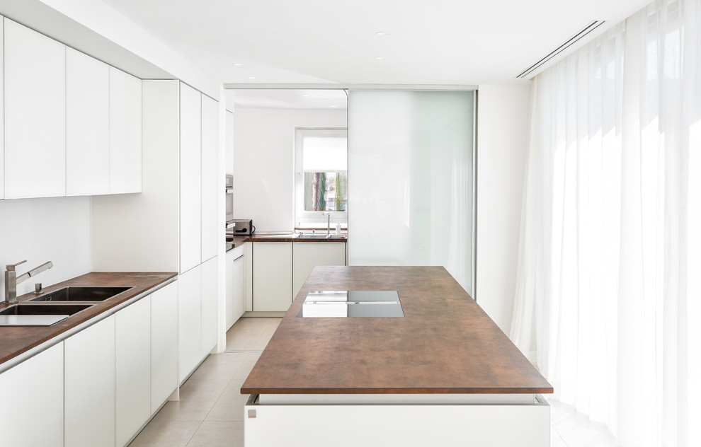 Photo of a medium sized mediterranean l-shaped kitchen in Munich with flat-panel cabinets, white cabinets, an island, a double-bowl sink, stainless steel appliances, ceramic flooring and beige floors.