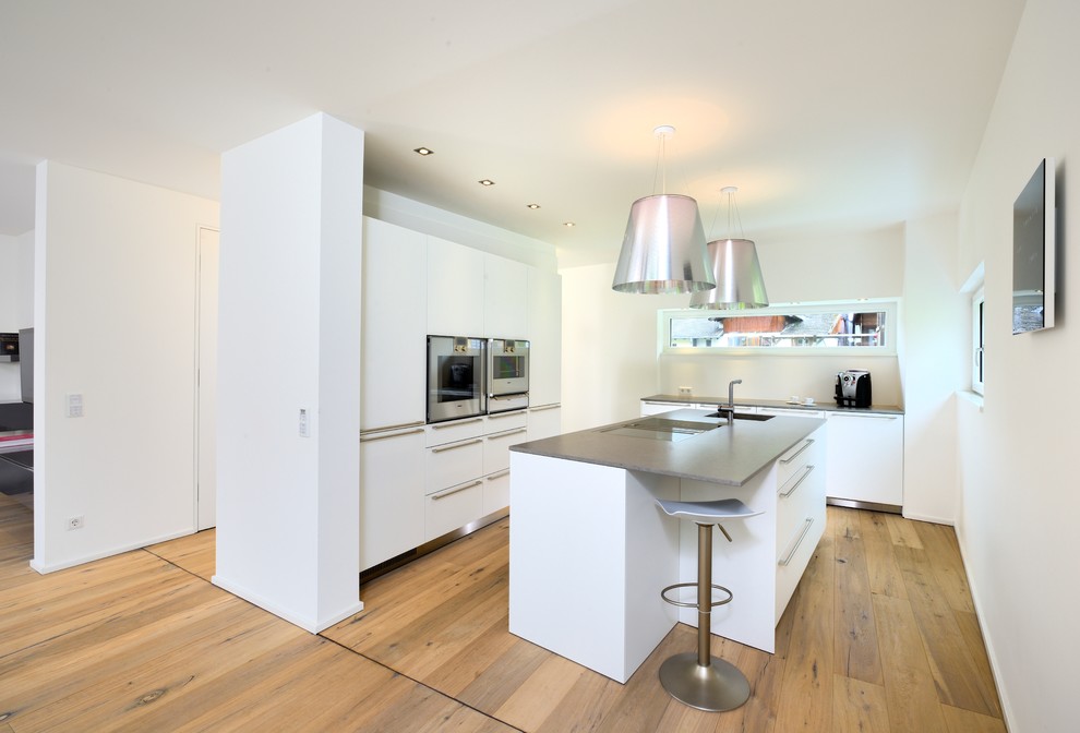 ミュンヘンにある中くらいなコンテンポラリースタイルのおしゃれなキッチン (一体型シンク、フラットパネル扉のキャビネット、白いキャビネット、パネルと同色の調理設備、無垢フローリング) の写真