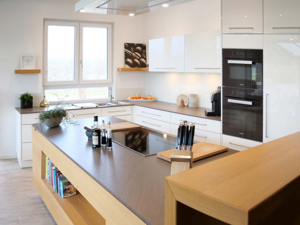 Photo of a large contemporary l-shaped open plan kitchen in Other with an integrated sink, flat-panel cabinets, white splashback, black appliances, laminate floors, an island, grey floors and grey worktops.
