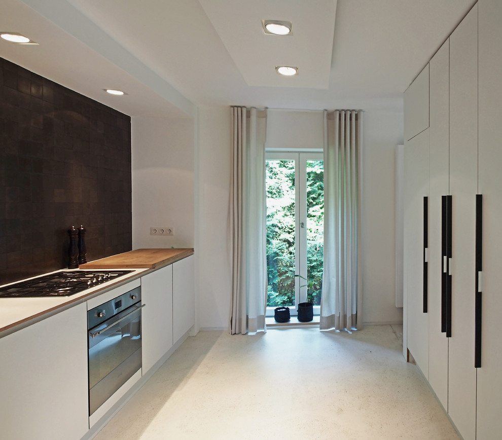 Exemple d'une petite cuisine linéaire tendance fermée avec un placard à porte plane, des portes de placard blanches, une crédence noire et un électroménager en acier inoxydable.