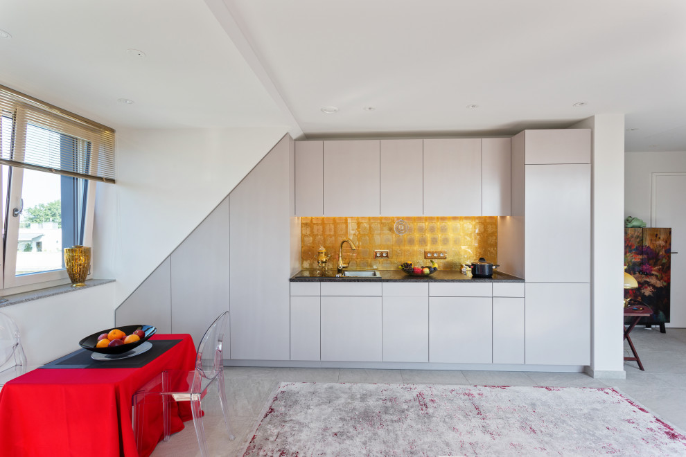 Moderne Küche mit Einbauwaschbecken, flächenbündigen Schrankfronten, weißen Schränken, Küchenrückwand in Metallic, Elektrogeräten mit Frontblende, grauem Boden und schwarzer Arbeitsplatte in München