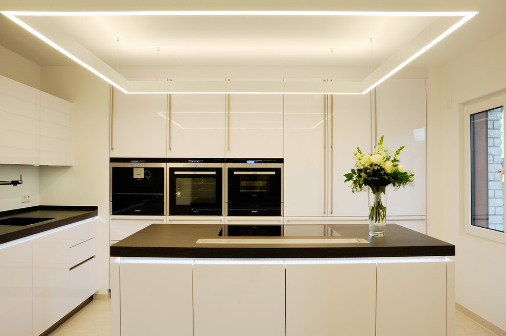 Immagine di una cucina design di medie dimensioni con lavello integrato, ante lisce, ante bianche, paraspruzzi bianco, paraspruzzi con lastra di vetro e elettrodomestici in acciaio inossidabile