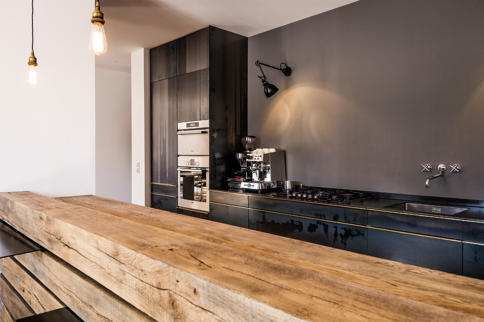Foto på ett mellanstort funkis kök, med släta luckor, skåp i slitet trä, en integrerad diskho, träbänkskiva, grått stänkskydd, rostfria vitvaror, mellanmörkt trägolv och brunt golv