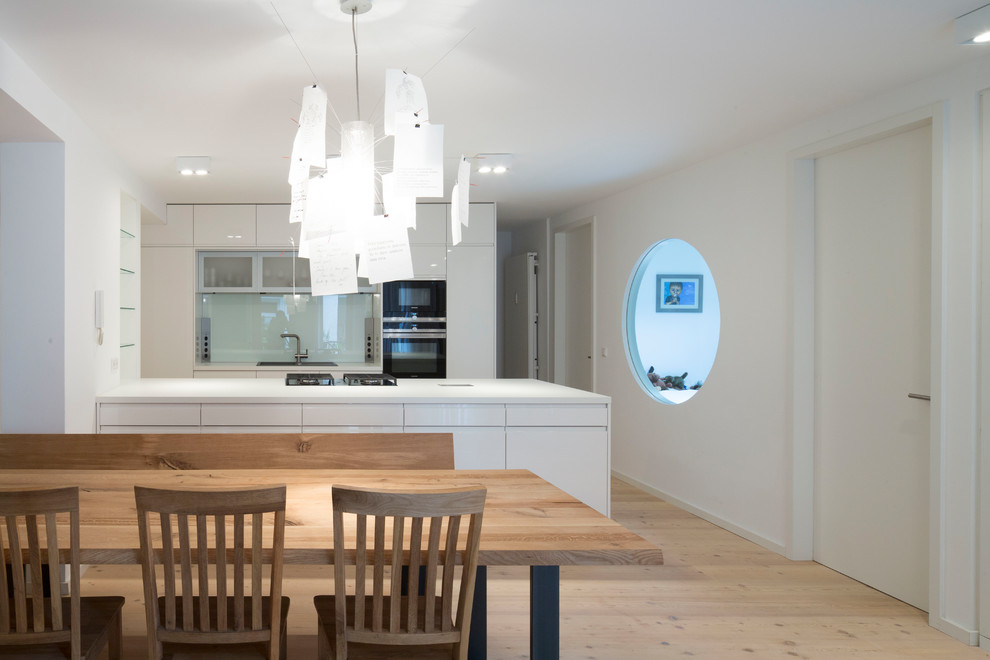 Eat-in kitchen - mid-sized modern galley light wood floor and beige floor eat-in kitchen idea in Munich with a drop-in sink, flat-panel cabinets, white cabinets, green backsplash, glass sheet backsplash, black appliances, a peninsula and white countertops