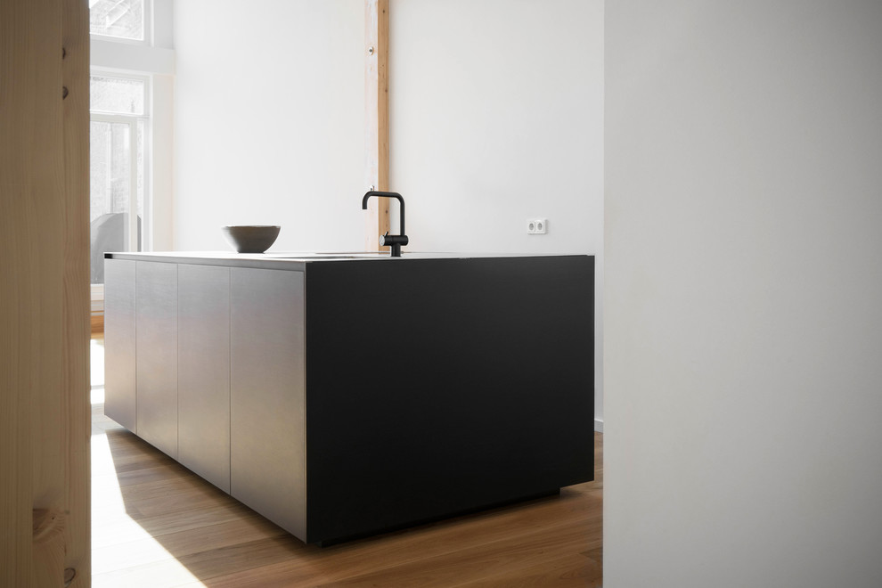 Design ideas for a medium sized modern single-wall kitchen/diner in Berlin with a submerged sink, flat-panel cabinets, black cabinets, stainless steel worktops, light hardwood flooring and an island.